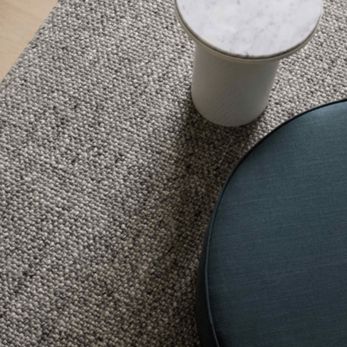 A close up of a grey wool rug with a white coffee table sitting on top.