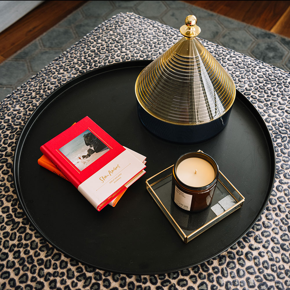 A circle tray with books, a candle and a container sitting on top.