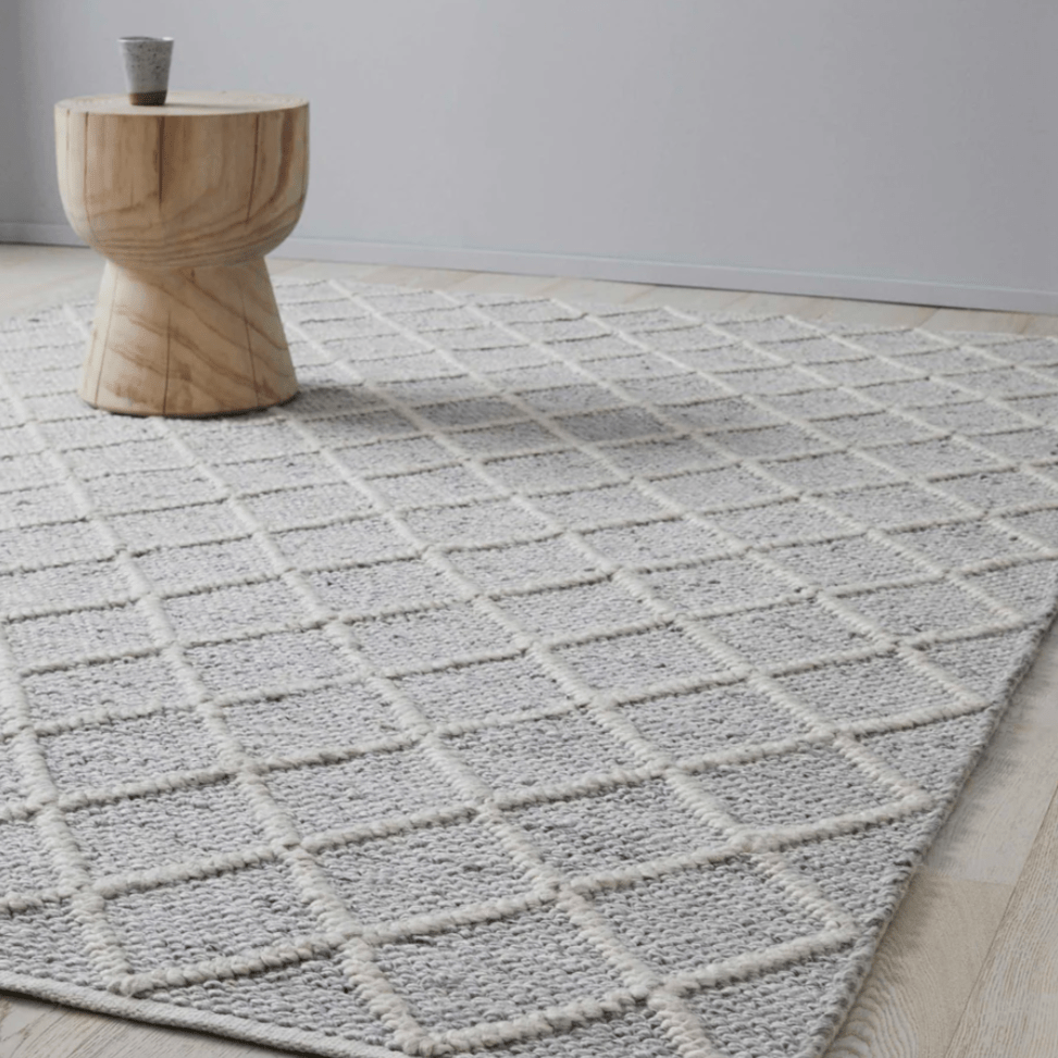 A grey wool rug with white raised patterns with a wooden circle coffee table sitting on top of it.