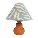 Table lamp with a zebra-patterned shade on an orange base against a white background