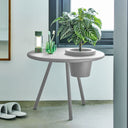 Round gray side table with a plant and glasses in a room with a window.