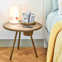 Round side table with lamp, books, and phone next to a bed.