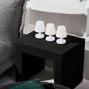 Three white lamps on a black side table next to a gray sofa.