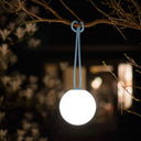 Glowing spherical light fixture hanging from a branch at night.
