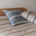 A styled bedroom scene showing striped bedding and pillows on a bed with a light wood headboard against a plain wall.