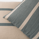 A close-up of a striped throw pillow in textured blue-gray and cream fabric, resting on a matching beige linen-textured surface.
