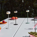 Three small outdoor Fatboy Cheerio table lamps on a table with food and drinks in an outdoor setting.