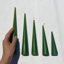Set of green taper candles on a white background with a hand for scale.