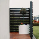 White planter with a plant on a wooden deck next to a black slatted screen.