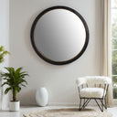 Round mirror with black frame on a white wall above a white chair and plant.
