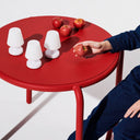 Red table with white lampshades and apples, person reaching for an apple.