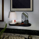 Small table on a black wallmount base with a mirror and decorative items against a white wall.