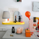 Desk with colorful items including a white lamp on a yellow wall mount base, candles, and decorative objects.