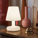 White lamp with a visible Fatboy brand label on a wooden surface with decorative vases in the background.