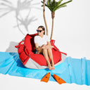 Woman sitting on a red and gray beanbag with palm trees in the background