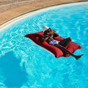 Person lounging on a red flaoting beanbag in a swimming pool.