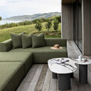 Green outdoor sofa with cushions on a wooden deck with a scenic view.