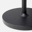 Close-up of a black round base with a matching black cylindrical leg centered on a light gray background.