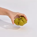 Hand holding a green tomato candle against a white background