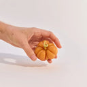 Hand holding a small orange tomato candle against a light background