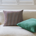 A striped throw pillow in vertical stripes of burgundy, navy, light blue, and cream sits on a textured beige sofa next to a solid green pillow.
