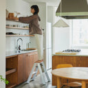 Person using the Lucano step stool to reach shelves in a modern kitchen.