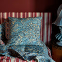 Blue patterned pillow and blanket on a striped sofa with a lamp in the corner.