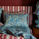 Floral-patterned pillows on a striped bed with a lamp in the corner.