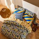 Bed with blue and green floral patterned bedding and pillows in a room with a lamp and rug.