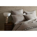 Neatly made bed with beige bedding and pillows against a brick wall.