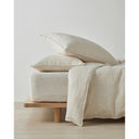 Beige linen bedding with linen pillows and duvet set on a wooden bed frame against a white wall