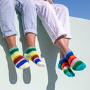 Two pairs of feet wearing colorful striped socks against a light blue background