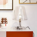 Clear glass table lamp on a white surface with a white wall in the background
