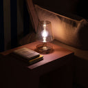 Small glass lamp on a wooden surface with a book underneath, in a dimly lit room.