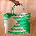 Woven green and beige bag held by a hand on a wooden surface