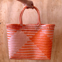 Woven basket with orange and white pattern held by a hand against a wooden background