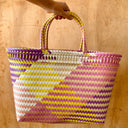 Colorful pink, yellow, purple, and beige woven bag with a geometric pattern held by a hand on a wooden surface
