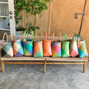 Colorful woven bags on a wooden bench outdoors.