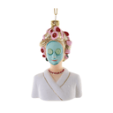 A decorative ornament shaped like a spa-themed woman bust, with a white robe, red beaded necklace, blue face mask, pink and gold hair rollers, and a gold hanging loop, shown on a plain white background.