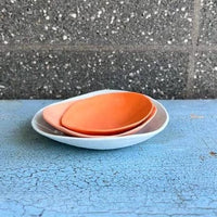 Side on view of a small orange ceramic bowl.