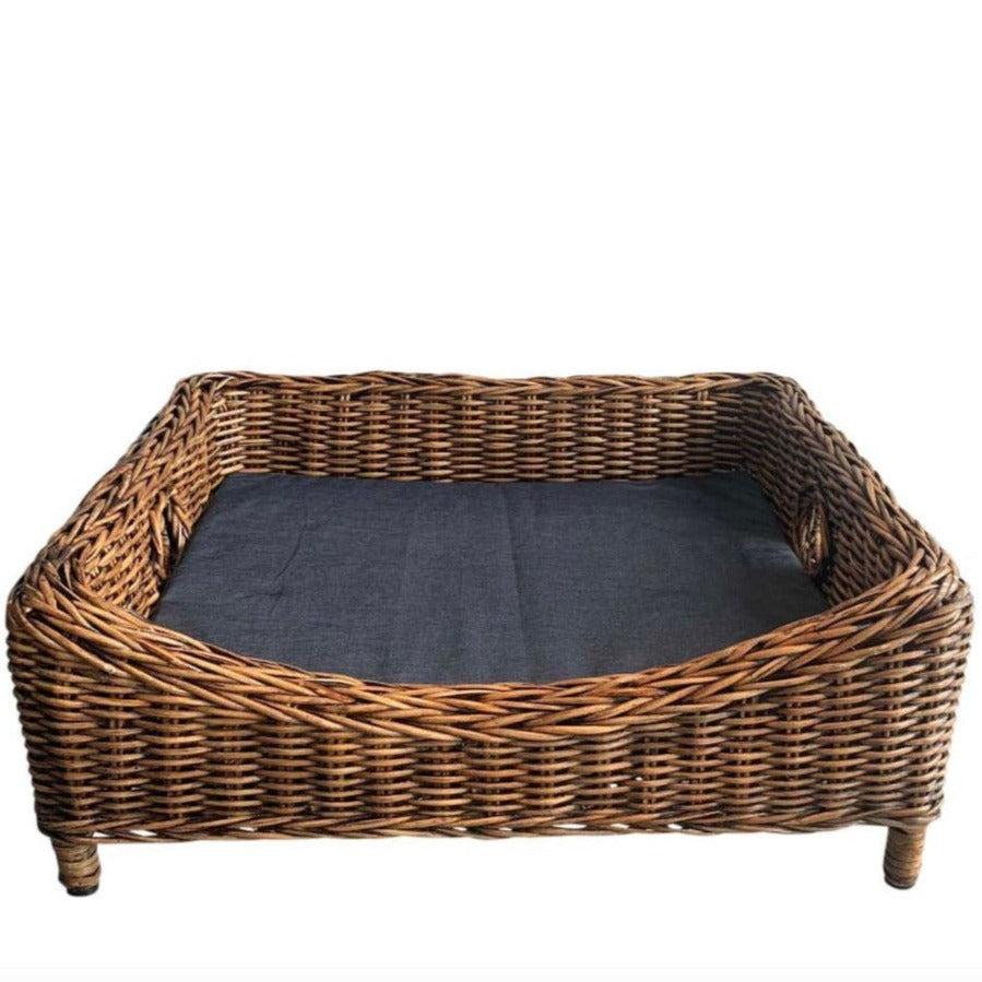 A small rattan square pet bed with a black cushion.