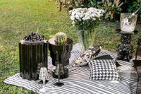 Black sottsass vases by Kartell sitting on a picnic blanket on the grass.