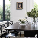 A white transparent centrepiece sitting on a wooden dining table with flowers sitting inside it.